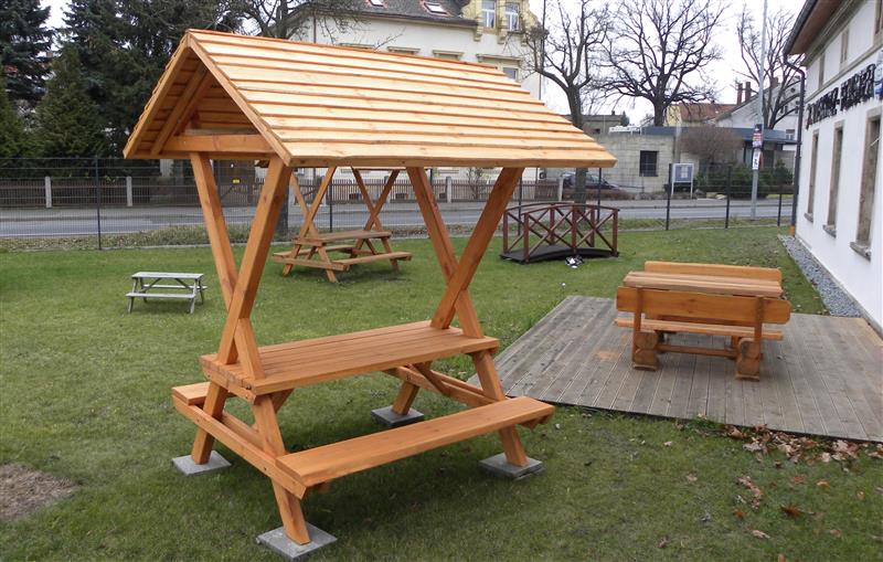 Überdachte Sitzgruppe aus Holz mit Tisch und zwei Bänken an den Seiten.