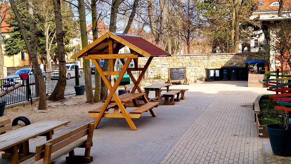 Die überdachte Sitzgruppe aus Holz steht neben anderen Bänken auf dem Schulhof.